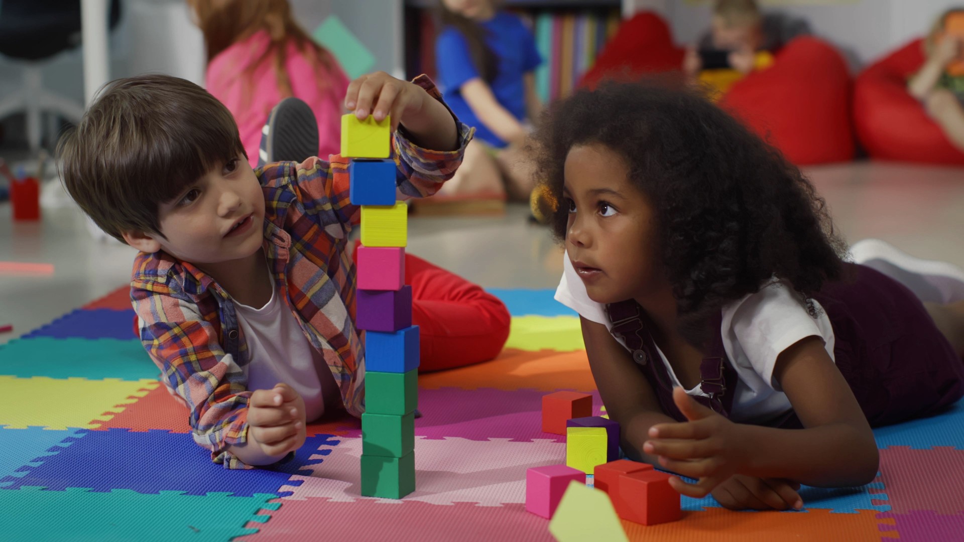 Cute multiethnic preschool kids playing with colored blocks on floor at nursery school